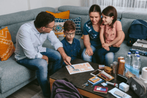 A family sits together on a couch, reviewing an emergency plan and go-bag supplies spread across the coffee table.