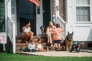 two women sitting on the front steps of a house talking and playing with their kids