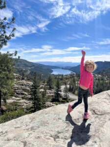 young girl on hike above a lake, posing for a photo